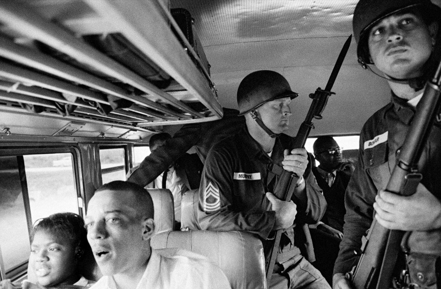 A photograph by Bruce Davidson, showing a bus used by supporters of the American Civil Rights, guarded my the army